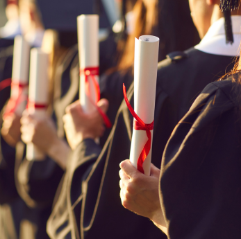 A row of graduates in black gowns and caps hold rolled diplomas tied with red ribbons during a gradu