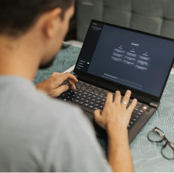 A person seen from behind types on a laptop displaying the ChatGPT interface, with glasses resting o
